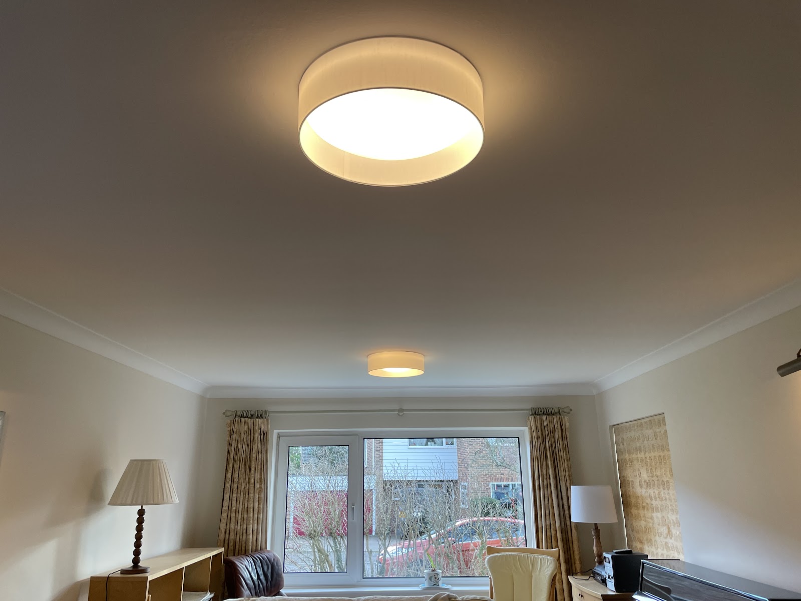 A pair of fabric drum ceiling lights fitted in a living room, hung level and balanced across the space.