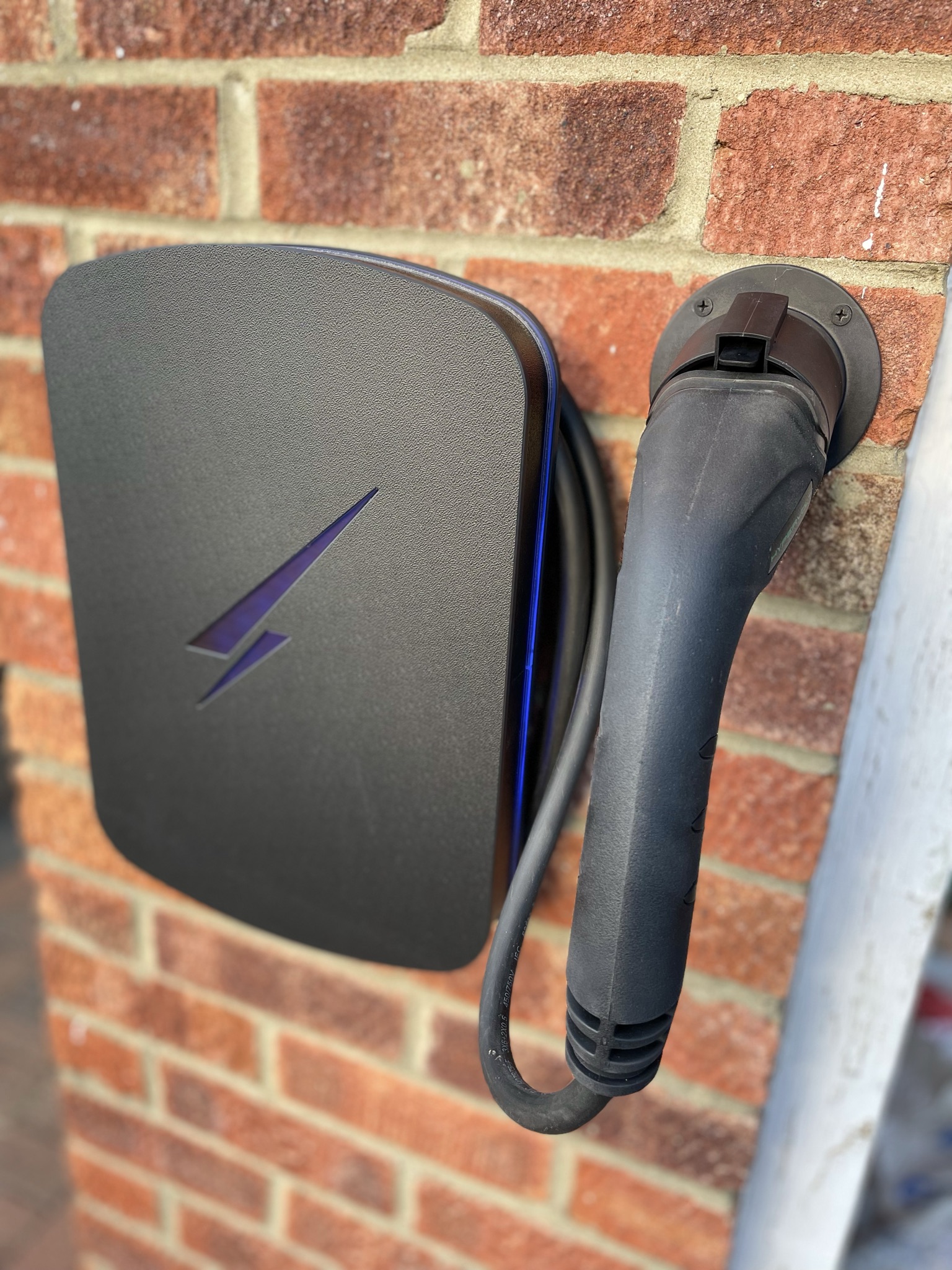 Dark chargepoint fitted flush to a brick wall, the tethered lead docked tidily in its holster.