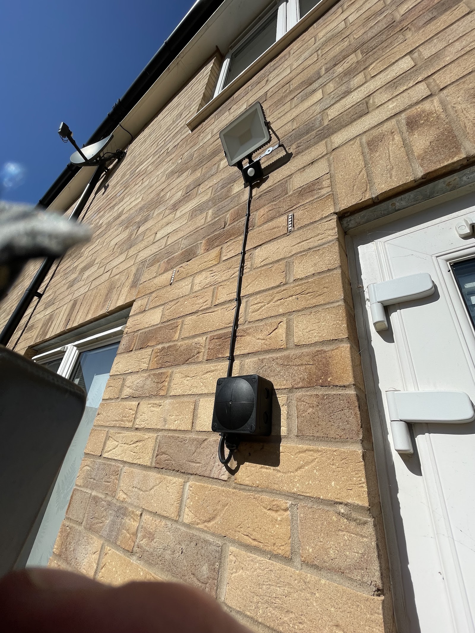 Exterior LED floodlight mounted high on a stone wall with a neat cable drop to a weatherproof enclosure.
